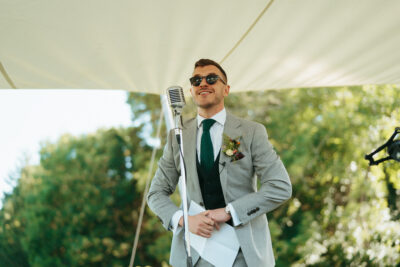 Man giving speech at outdoor wedding.
