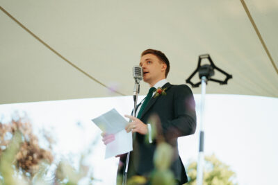 Man giving speech at outdoor event with microphone.