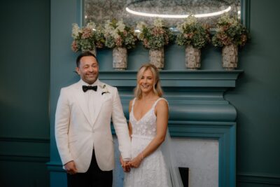 Smiling couple in wedding attire holding hands indoors.