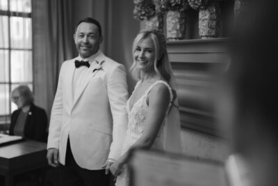 Smiling couple in wedding attire holding hands indoors.
