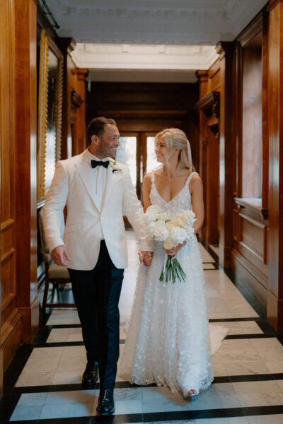 Couple smiling and holding hands in wedding attire.