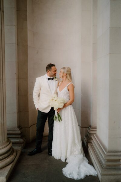 Bride and groom smiling, holding white roses.