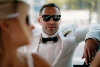 Person in sunglasses and white suit jacket.