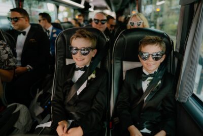 Children in suits wearing heart-shaped sunglasses on bus.