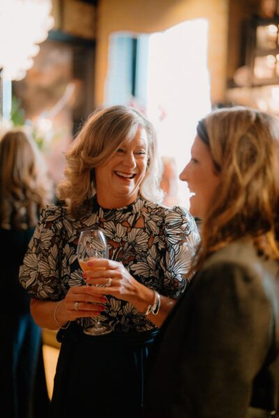 Women laughing, holding drinks at social event.
