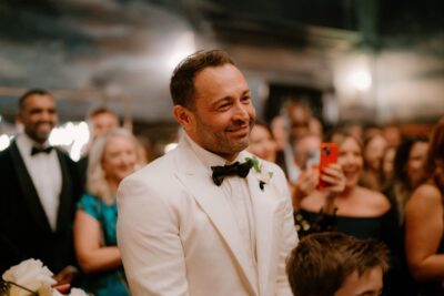 Smiling man in white suit at event.
