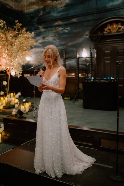 Woman in white dress giving speech at event.