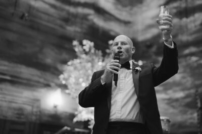 Man in suit giving a speech, holding a drink.