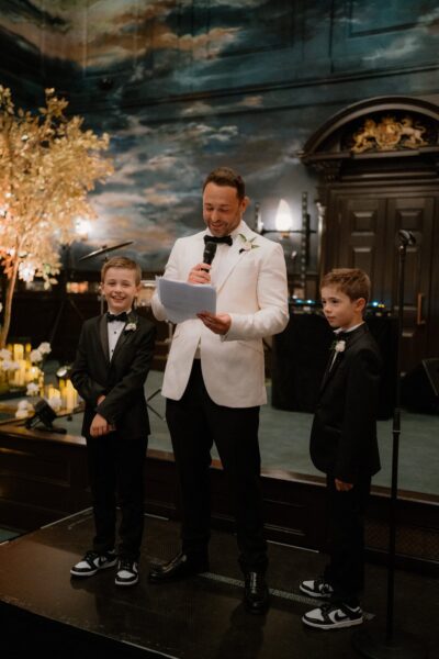 Man speaking with microphone, two boys in suits.