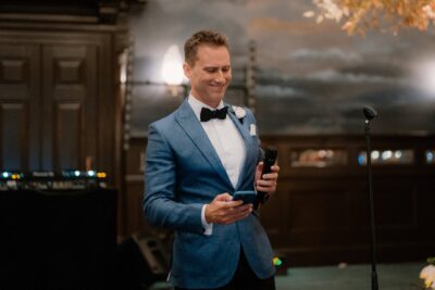 Man in blue suit smiling, holding microphone.