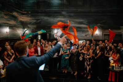 Celebratory crowd waving colourful flags indoors.