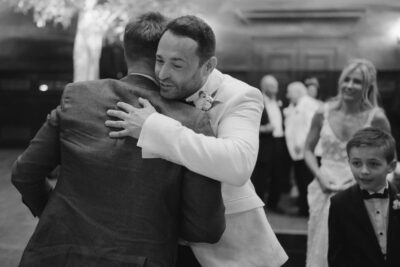 People hugging at a formal event, smiling, dressed elegantly.