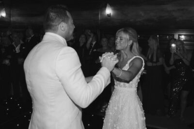 Couple dancing at wedding reception, smiling guests around.