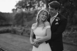 Couple smiling in wedding attire, embracing outdoors.