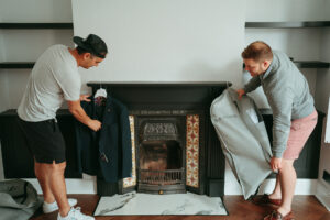 Two men examining suit by fireplace.