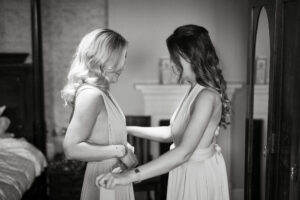 Two women in elegant dresses holding hands.