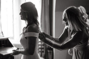 Bride getting ready, bridesmaid assisting, black and white photo.