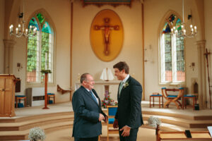 Two men smiling inside a church at a wedding.