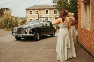 Bridesmaids by vintage car at wedding venue.