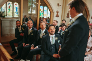 Groomsmen smiling in church at wedding ceremony.