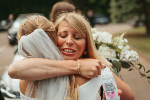 Bride embracing woman joyfully at wedding.