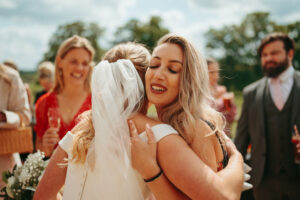 Bride embracing guest at sunny wedding ceremony.