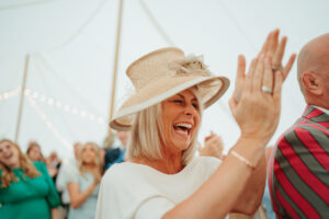 Woman in hat laughing, high-fiving at festive gathering.