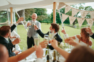 Wedding toast celebration under marquee in countryside.