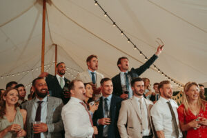 Wedding guests cheering in marquee with string lights.