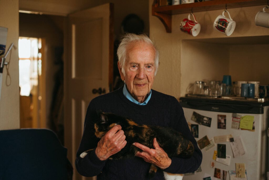 Elderly man holding cat in cozy kitchen.