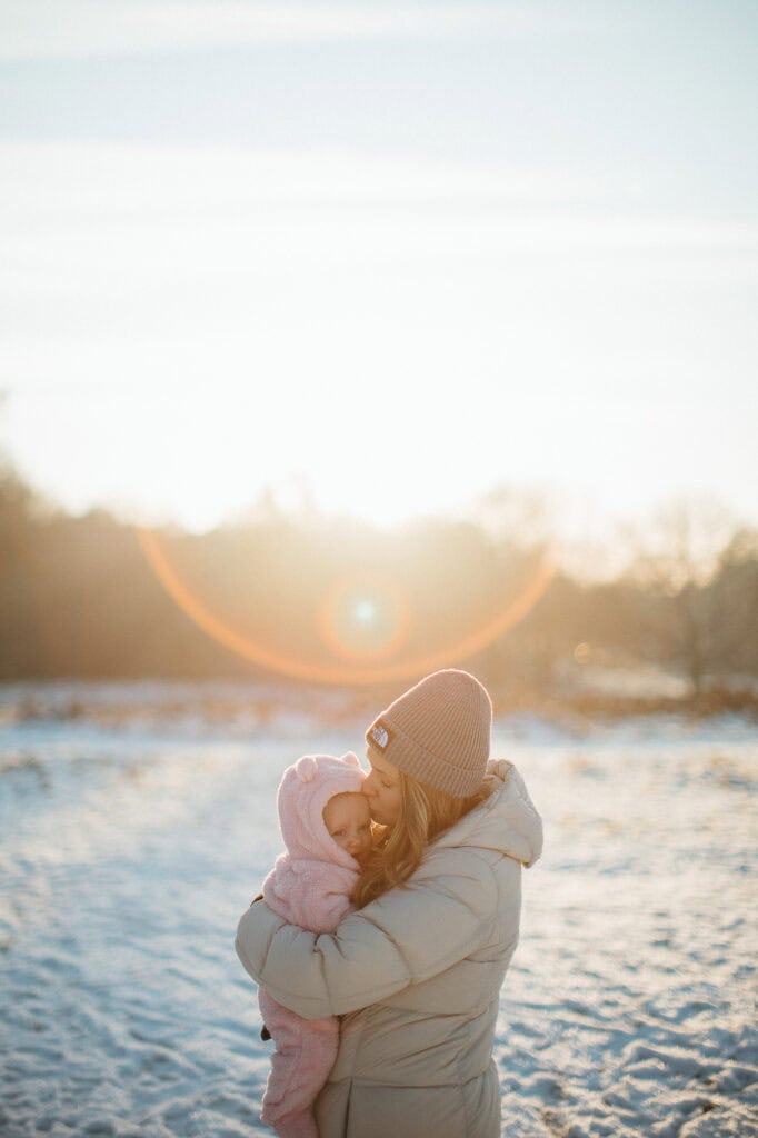 Mother embracing child in snowy landscape at sunset.