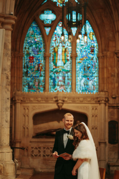 Bride and groom smiling in historic church with stained glass.