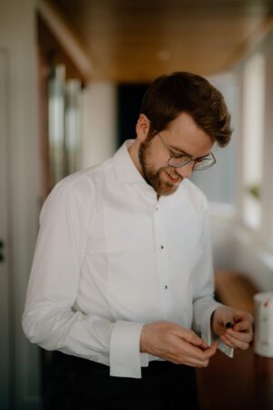 Man adjusting cufflinks wearing white shirt.