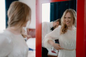 Woman smiling in mirror, adjusting dress belt.