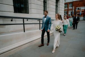 Bride and groom walking with friends outside building.