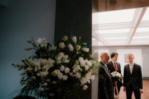 Three men in suits beside flower arrangement indoors.