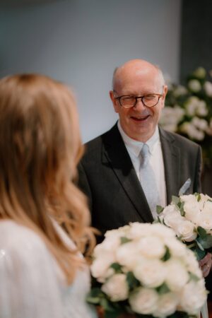 Man smiling, holding bouquet at wedding ceremony.