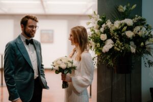 Couple smiling with wedding flowers indoors.