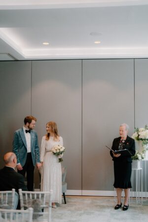 Couple holding hands at indoor wedding ceremony.