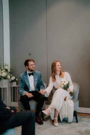 Bride and groom holding hands, sitting together.