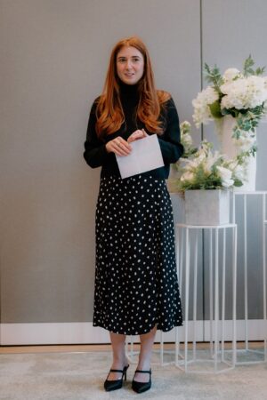 Woman holding paper next to floral arrangement indoors.