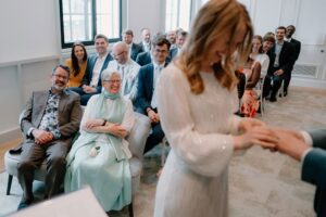 Bride exchanging rings, guests seated at wedding ceremony.