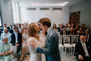 Couple kissing at wedding ceremony with guests watching.