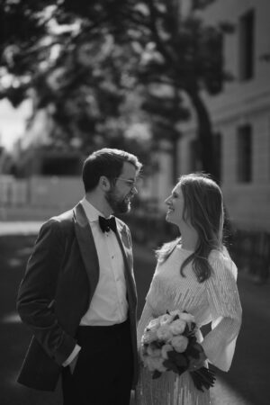 Smiling couple in elegant attire holding flowers.