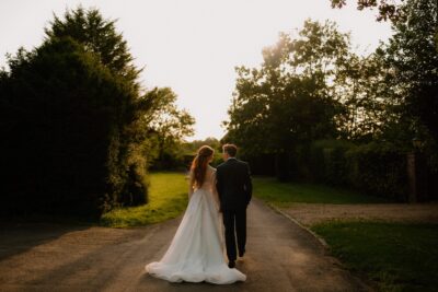 Bride and groom walking hand in hand at sunset.