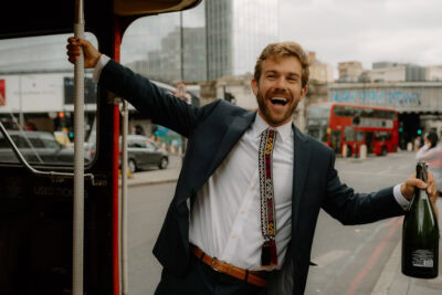Man celebrating on London street holding wine bottle.