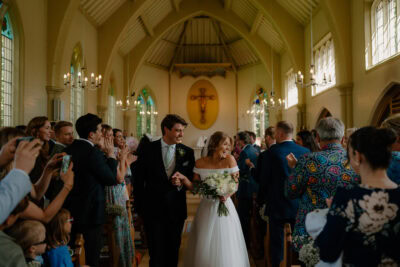 Bride and groom exiting church with guests applauding.
