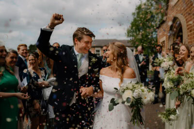 Happy couple celebrates wedding with confetti outside church.