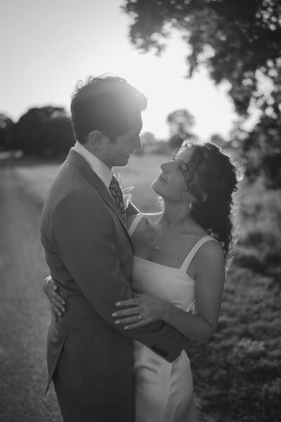 Couple embracing outdoors with sunlight in background.