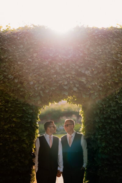Two men holding hands under sunlit archway.